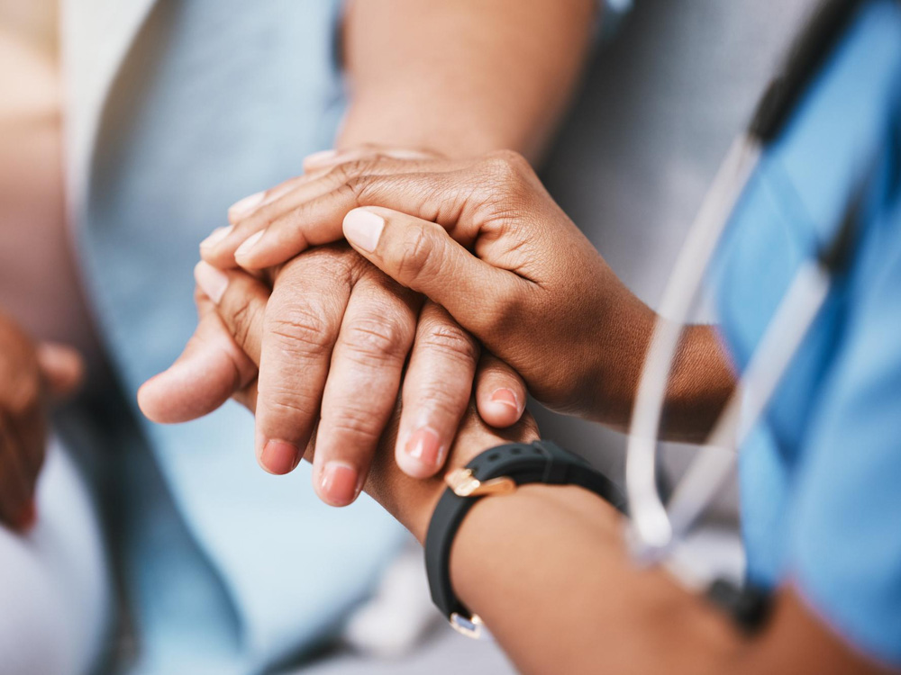 Healthcare professional holding a patient's hand in a comforting manner.