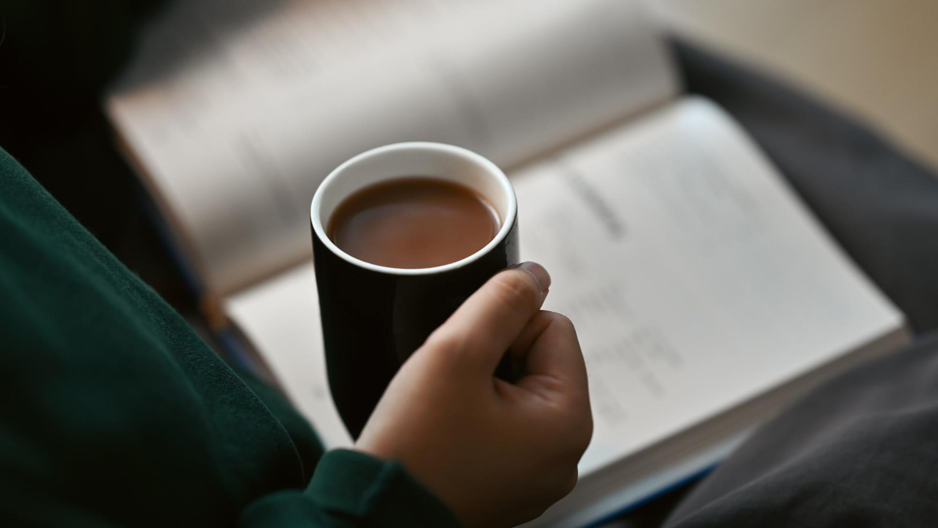 Person holding a mug of coffee while reading a book.